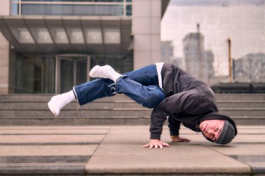 Genç, zinde bir yetişkin coşkuyla break dans yapıyor, amuda kalkıyor ve kendini kaldırıyor. Kot pantolon, şehir kıyafeti ve kep giymişti. Bir sürü tavır, hareket ve iyi enerji. Sokak dansı, serbest stil, modern dans..