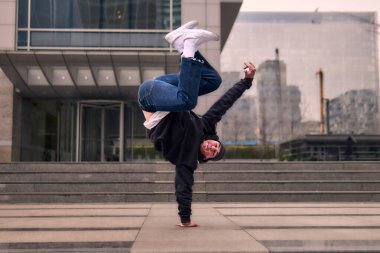 Genç, zinde bir yetişkin coşkuyla break dans yapıyor, amuda kalkıyor ve kendini kaldırıyor. Kot pantolon, şehir kıyafeti ve kep giymişti. Bir sürü tavır, hareket ve iyi enerji. Sokak dansı, serbest stil, modern dans..