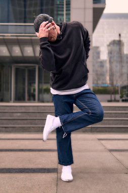 Genç ve zinde bir yetişkin kameraya poz vererek break dans yapıyor. Şehir kıyafeti ve kep giymişti. Bir sürü tavır, hareket ve iyi enerji. Sokak dansı, serbest stil, modern dans..