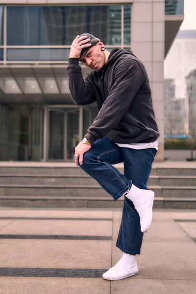 Genç ve zinde bir yetişkin kameraya poz vererek break dans yapıyor. Şehir kıyafeti ve kep giymişti. Bir sürü tavır, hareket ve iyi enerji. Sokak dansı, serbest stil, modern dans..