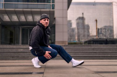 Genç ve zinde bir yetişkin kameraya poz vererek break dans yapıyor. Şehir kıyafeti ve kep giymişti. Bir sürü tavır, hareket ve iyi enerji. Sokak dansı, serbest stil, modern dans..