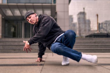 Genç ve zinde bir yetişkin kameraya poz vererek break dans yapıyor. Şehir kıyafeti ve kep giymişti. Bir sürü tavır, hareket ve iyi enerji. Sokak dansı, serbest stil, modern dans..