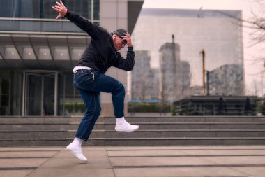 Genç bir yetişkin hip hop break dansı yapıyor, sokaklarda coşkuyla zıplıyor ve dans ediyor. Rahat kıyafetler giyer ve tutum, hareket ve pozitif enerji yayar. Sokak dansı, serbest stil, modern dans..
