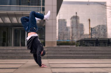 Genç, zinde bir yetişkin coşkuyla break dans yapıyor, amuda kalkıyor ve kendini kaldırıyor. Kot pantolon, şehir kıyafeti ve kep giymişti. Bir sürü tavır, hareket ve iyi enerji. Sokak dansı, serbest stil, modern dans..