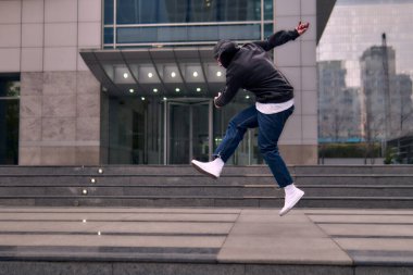 Genç bir yetişkin hip hop break dansı yapıyor, sokaklarda coşkuyla zıplıyor ve dans ediyor. Rahat kıyafetler giyer ve tutum, hareket ve pozitif enerji yayar. Sokak dansı, serbest stil, modern dans..
