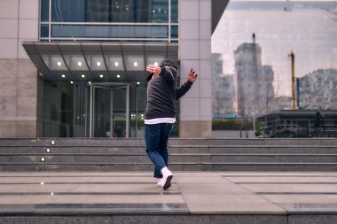 Formda bir genç adam coşkuyla break dans yapar, sert adam pozları verir, şınav çeker ve ritme ayak uydurur. Kot pantolon, sokak kıyafeti ve şapka giyiyor. Tavır, hareket ve enerji dolu. Sokak dansı, serbest stil ve modern dans..