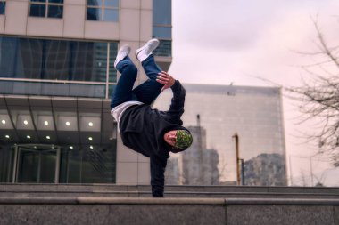 Genç, zinde bir yetişkin coşkuyla break dans yapıyor, amuda kalkıyor ve kendini kaldırıyor. Kot pantolon, şehir kıyafeti ve kep giymişti. Bir sürü tavır, hareket ve iyi enerji. Sokak dansı, serbest stil, modern dans..