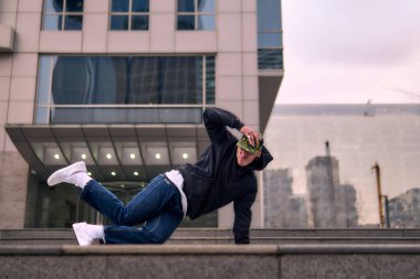 Genç, zinde bir yetişkin coşkuyla break dans yapıyor, amuda kalkıyor ve kendini kaldırıyor. Kot pantolon, şehir kıyafeti ve kep giymişti. Bir sürü tavır, hareket ve iyi enerji. Sokak dansı, serbest stil, modern dans..