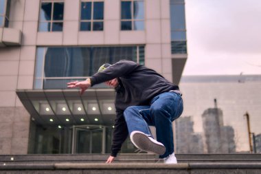 Genç, zinde bir yetişkin coşkuyla break dans yapıyor, amuda kalkıyor ve kendini kaldırıyor. Kot pantolon, şehir kıyafeti ve kep giymişti. Bir sürü tavır, hareket ve iyi enerji. Sokak dansı, serbest stil, modern dans..