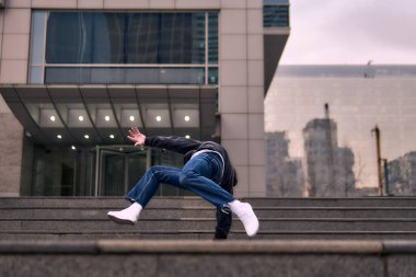 Genç, zinde bir yetişkin coşkuyla break dans yapıyor, amuda kalkıyor ve kendini kaldırıyor. Kot pantolon, şehir kıyafeti ve kep giymişti. Bir sürü tavır, hareket ve iyi enerji. Sokak dansı, serbest stil, modern dans..