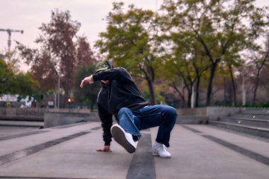 Genç yetişkinler coşkuyla dans eder, amuda kalkar ve yerde döner. Kot pantolon, sokak kıyafeti ve şapka giyiyor. Bir sürü tavır, hareket ve iyi enerji. Sokak dansı, serbest stil ve modern dans..