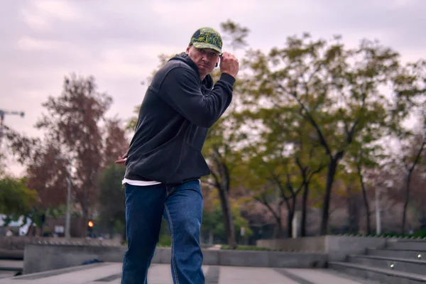 Genç, atletik bir adam şehirde coşkuyla dans ediyor, sert çocuk pozları veriyor ve ritme ayak uyduruyor. Kot pantolon, sokak kıyafetleri ve şapka giyiyor. Tavır, hareket ve iyi enerji yayıyor. Sokak dansı, serbest stil ve modern dans..