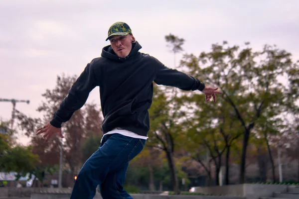 Genç, atletik bir adam şehirde coşkuyla dans ediyor, sert çocuk pozları veriyor ve ritme ayak uyduruyor. Kot pantolon, sokak kıyafetleri ve şapka giyiyor. Tavır, hareket ve iyi enerji yayıyor. Sokak dansı, serbest stil ve modern dans..