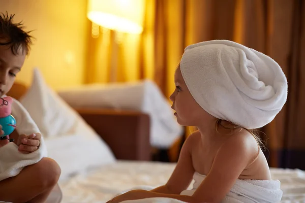 Niño y hermana con el pelo mojado bajo las toallas sobre la cama — Foto de Stock