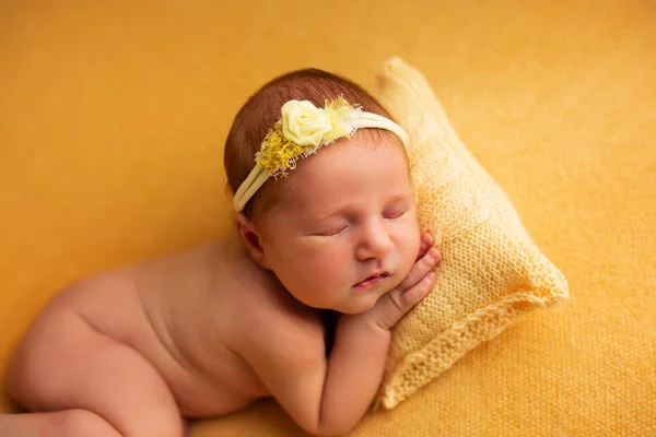 portrait of a beautiful seven day old baby girl. She is sleeping in a curled up fetal position on a yellow blanket