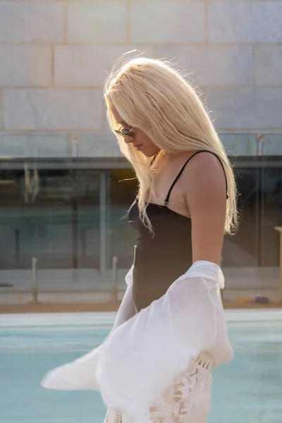 Porträtt av ung vacker sexig solbränd smal blond kvinna i solglasögon dans nära poolen i svart baddräkt — Stockfoto
