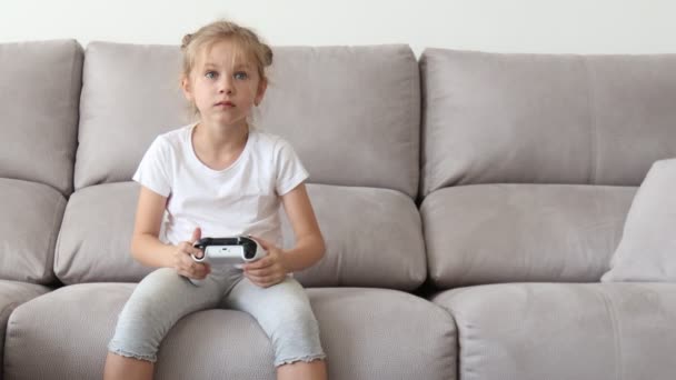 Lelkes srác alkalmi ruhában játszik joystick, miközben ül a kanapén a nappaliban. — Stock videók