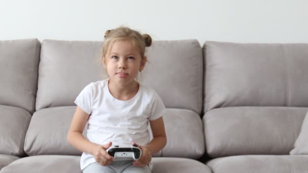 Evde bilgisayar ekranının önünde kumandalı joysticklerle oynayan sevimli küçük bir kız. — Stok video