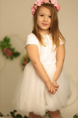 Bej arka planda 3-4 yaşlarında gülümseyen bir bebek. Çiçekli çelenk giyiyordu. Kameraya bakıyorum. Çocukluk. Zarafet