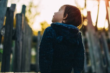 Küçük kız tahta bir kaydırağın üzerinde oturuyor sırtı ve gökyüzüne bakıyor.
