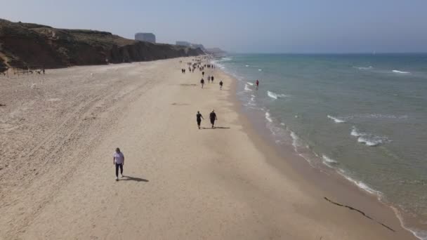 Herzliya, Israel - 18 de abril de 2021: locales a pie, costa mediterránea, playa desde el muelle. Marea de olas de agua de mar, arena costera. Resort hotel junto al mar. El terraplén — Vídeos de Stock