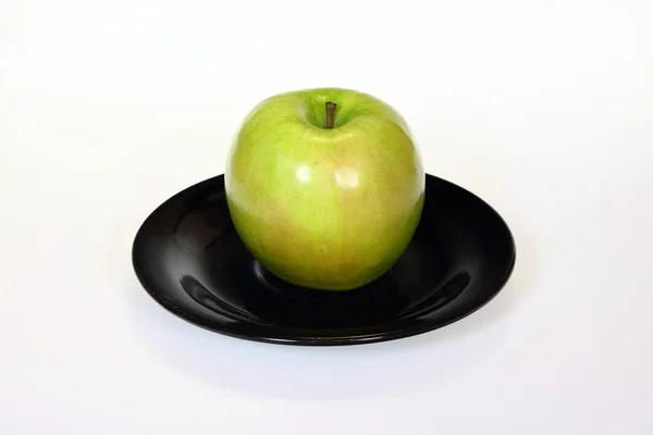 Зеленое яблоко на черной тарелке, изолированной на белом — стоковое фото