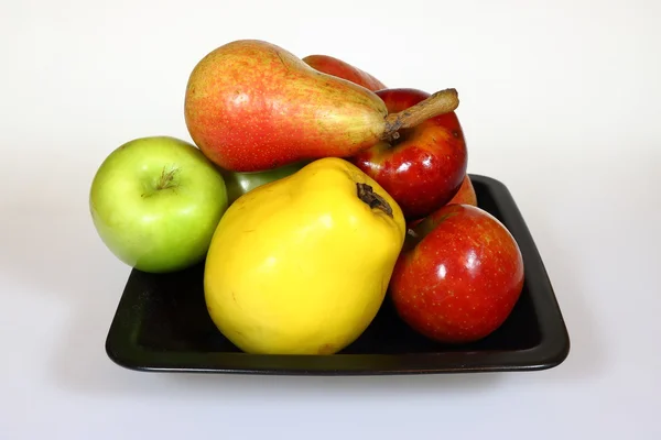 Fruits sur une assiette noire : poires rouges, pommes rouges et vertes, coing isolé sur blanc — Photo