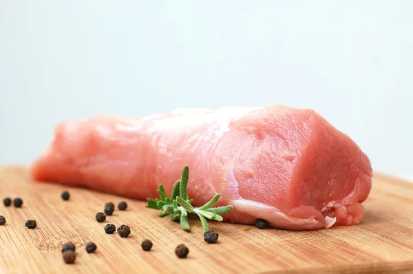 Rohes Schweinefilet mit schwarzem Pfeffer und Rosmarin auf zum Kochen zubereitetem Holz — Stockfoto