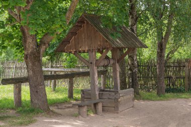 Dallanan ağaçların gölgesinde bir bankı olan kırsal bir kuyu. Stok Fotoğrafı