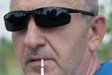 Siyah güneş gözlüklü bir adamın yüzü, yakın plan sigarası, bulanık arka plan ve bokeh elementleri. Stok fotoğrafçılığı.