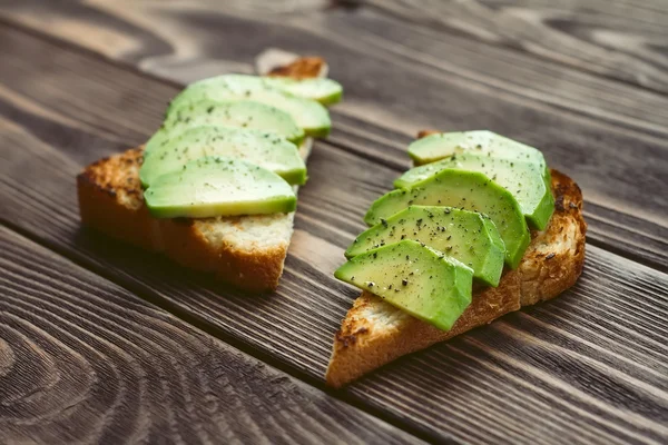 Toast for two persons with fresh avocado and pepper on a wooden table — Stock Photo, Image