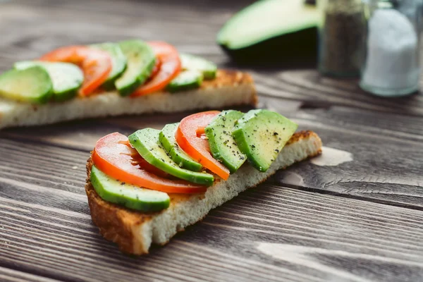 Sandwich καλοκαιρινό χρώμα με κόκκινη ντομάτα και πράσινη φέτες αβοκάντο σε ένα ξύλινο τραπέζι. — Φωτογραφία Αρχείου