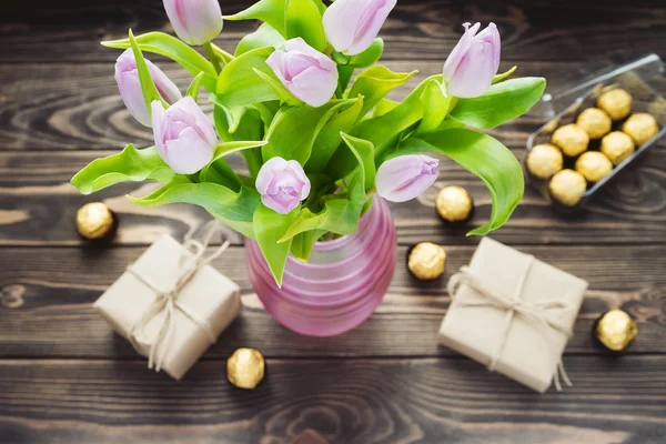 Bouquet of purple tulip in the pink vase with gift boxes and candies — Stock Photo, Image