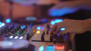 Profesyonel bir karıştırma konsolu ve renkli LED ışıkları üzerindeki kontrolleri ayarlayan DJ ellerinin yakın çekimi. Dinamik parti atmosferi, müzik performansı, gece hayatı, modern girişim konsepti..