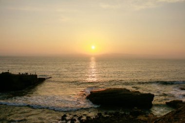 Sahilde gün batımı, kayalıkları ve denizde batan güneşi görebilirsiniz..