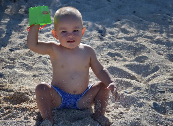 Neşeli küçük bir çocuk sıcak deniz kumlarında oynar ve dinlenmekten zevk alır.