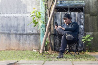 Arka bahçesinde cep telefonu olan bir adam oturuyor.