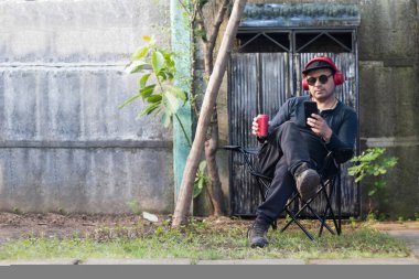 Arka bahçesinde oturan Latin adam cep telefonuna bakıyor.