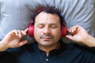 Yatağa uzanmış müzik dinleyen, rahatlamış bir adam.