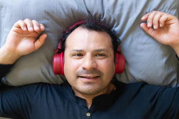 Latin bir adam yatağa uzanıp kulaklıkla müzik dinlemeyi sever.