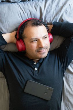 Rahat bir adam yatağında müzik dinliyor.