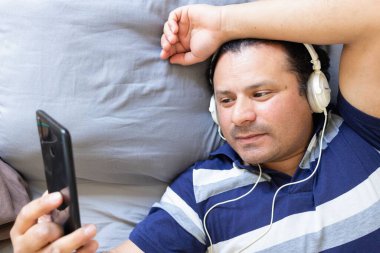 Adam yatakta yatarken telefonunu kontrol ediyor.