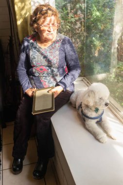 Yaşlı bir kadın pencerenin kenarında bir kanişin yanında oturuyor.