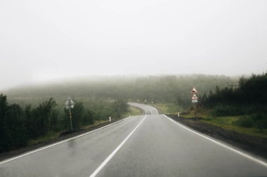 Murmansk region - August 2018: Panoramic view of the misty asphalt road in rainy weather. Foggy winding highway surrounded by mountains and hills in Kola Peninsula. Summer morning road and fog.