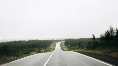 Murmansk region - August 2018: Panoramic view of the misty asphalt road in rainy weather. Foggy winding highway surrounded by mountains and hills in Kola Peninsula. Summer morning road and fog.