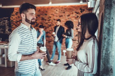 Ofis duvarında elinde kahve fincanlarıyla dikilmiş iki mutlu iş arkadaşı konuşuyor..