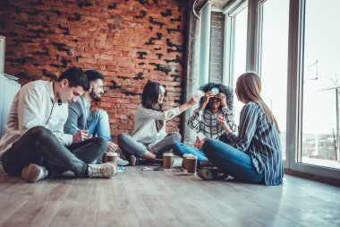 Ofisin zemininde otururken ve alnında kağıt çıkartmalarla oyunlar oynarken, birlikte ve takım ruhuyla eğlenen genç iş arkadaşları. Alt görünüm