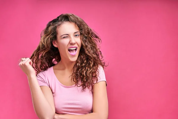 Pretty young woman winking, smiling at the pink background. Copy space