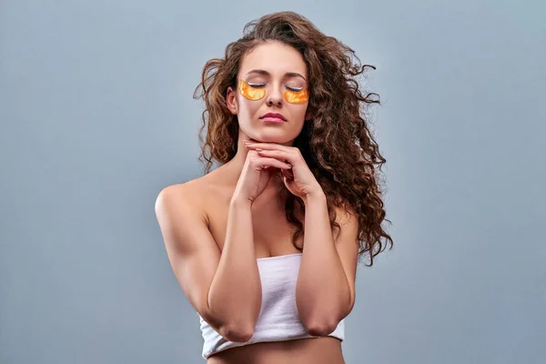 Eye skin treatment with gel patch. Young woman with golden patch on face. Isolated on grey.