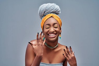 Gri arka planda kapalı gözleri olan mutlu Afro-Amerikan genç kadın.